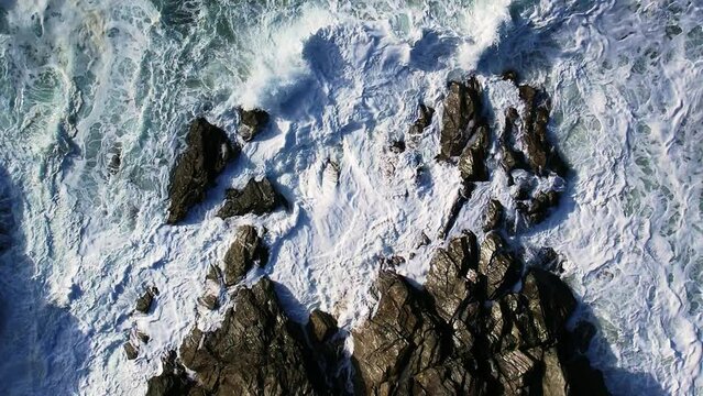 Aerial Top Down of White Ocean Waves Over Cornish Rocks in Cornwall. Slow Rotating Drone Shot.