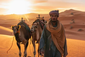 Rolgordijnen Berber man leading camel caravan at sunset. A man leads two camels through the desert © Kien