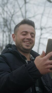 Vertical video. Short-haired, Fair-skinned Young Man Having a Video Chat on his Smartphone Outdoors	