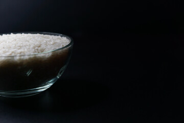 uncooked rice in a bowl isolated on a black background, copy space.