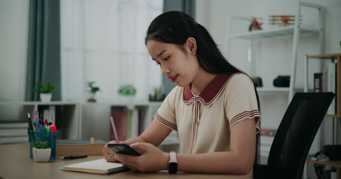 Footage dolly shot, Selective focus,Happy young asian woman sitting at desk writing noting information to diary from smartphone at home, creative thoughts to journaling