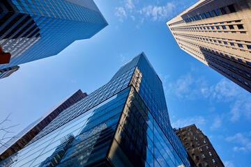 Looking up at tall buildings with many stories against a bright blue sky in New York City USA
