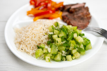 Meal. Green salsa tomatillo. Fajita, sweet bell peppers, onions, beef ribeye steak grilled on charcoal and Basmati rice. Cooked meat and vegetables. Healthy dinner. Plate on white natural wooden table