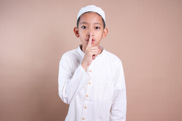 Asian muslim little boy holding forefinger on his lips asking for silence