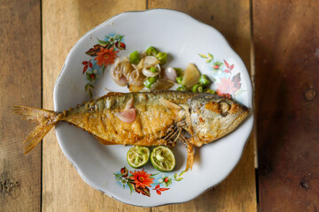 Ikan Peda  or ikan asin fried with sliced chili peppers, onions, and lime, served on a white plate.