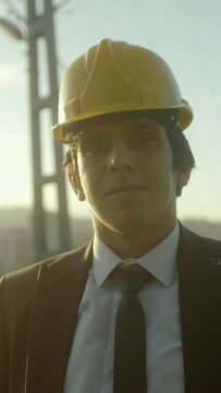 Vertical video. A Young, Handsome, Suit-and-Tie-Clad, Beardless, Helmeted Businessman or Urban Planner Smiling at the Camera with a Cityscape Background	
