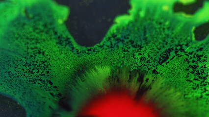 Paint drop. Ink spill. Defocused red green black color glowing fluid splash spreading flow motion particles texture dark abstract background.