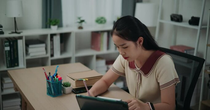 Footage dolly and high angle view shot, Happy young asian woman sitting at desk writing notes while working on tablet for online learning at home, creative thoughts to journaling, idea and inspiration