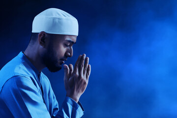 Portrait of sad crying young asian muslim man with beard praying on dark blue background - 739687114