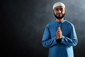Portrait of handsome young asian muslim man with beard greeting hand gesture and smiling isolated on dark background - 739687563