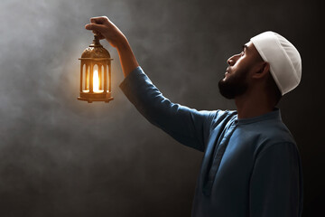 Young asian muslim man with beard holding arabic lantern looking up on dark background at night - 739687733