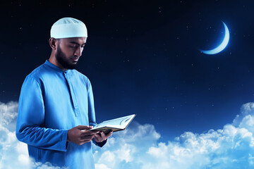 Young asian muslim man with beard reading holy book quran at blue night sky with stars and crescent moon - 739687983