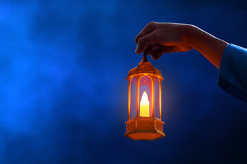Hands of young asian muslim man holding shiny arabic lantern on dark blue background at night - 739688529