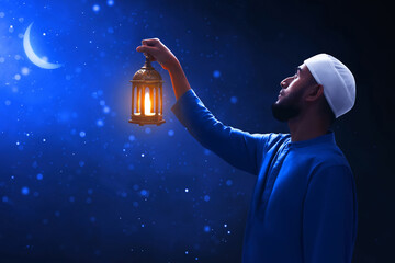 Young asian muslim man with beard holding arabic lantern looking at beautiful blue night sky with stars and crescent moon - 739688570