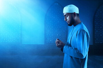 Young asian muslim man with beard praying in the mosque window arch at dark night - 739689388