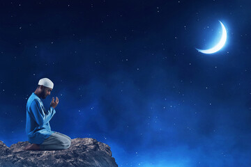Fototapeta na wymiar Young asian muslim man with beard praying , sitting on on top rock monuntain at beautiful blue night sky with stars and moon