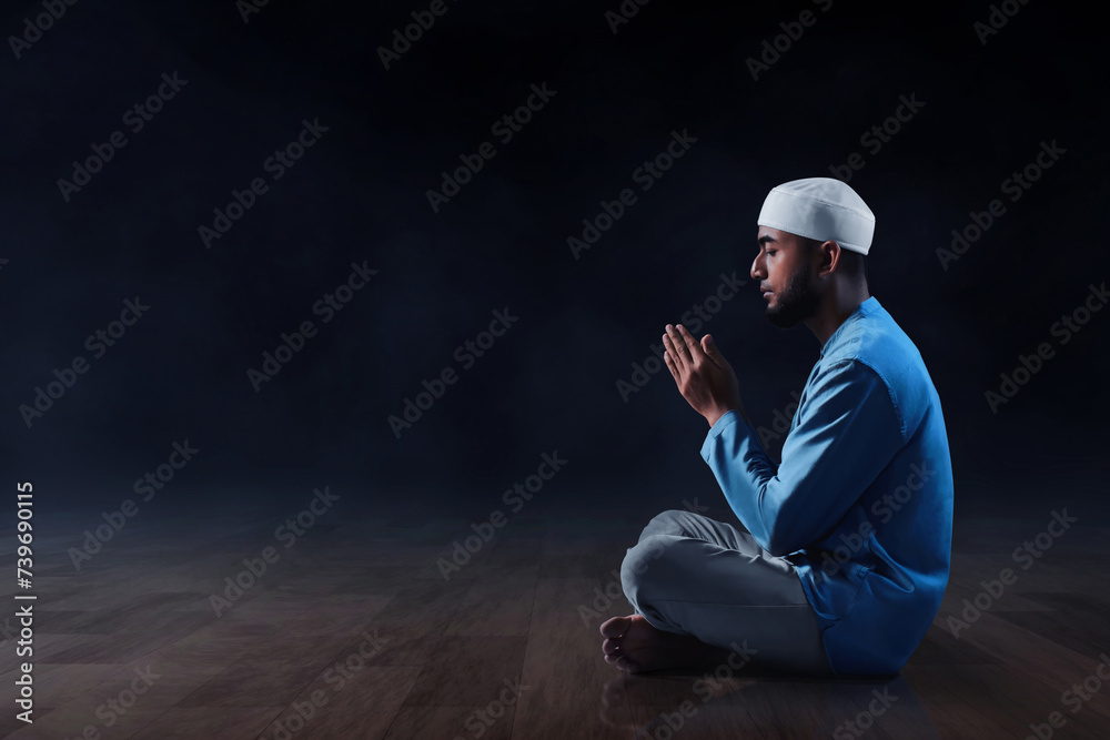 Wall mural Young asian muslim man with beard praying on dark background