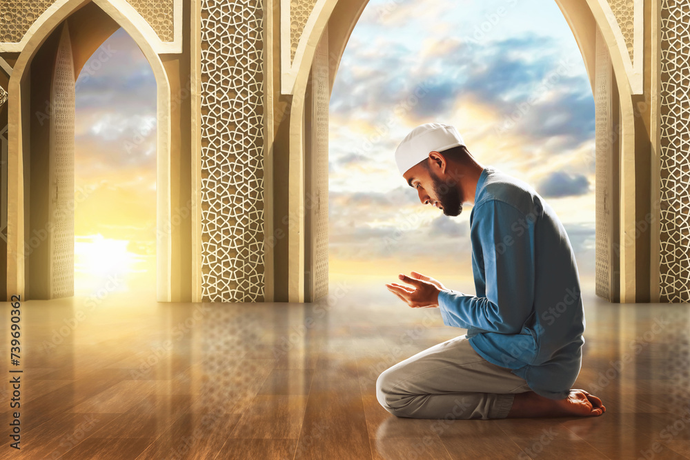 Wall mural Young asian muslim man with beard praying in the mosque door arch at beautiful sunset sky