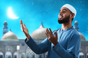 Portrait of handsome young asian muslim man with beard greeting gesture, thankful and smiling at blue night sky with stars and crescent moon - 739691770