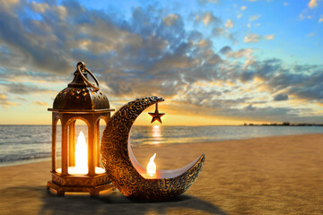 Shiny golden crescent moon with star lantern and arabic lantern on sea beach at beautiful sunset...