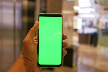 holding smart phone with green screen against shopping mall background 