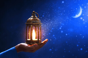 Hands of young asian muslim man holding shiny arabic lantern at blue night sky with stars and crescent moon, with glitter and sparkle effect - 739694995