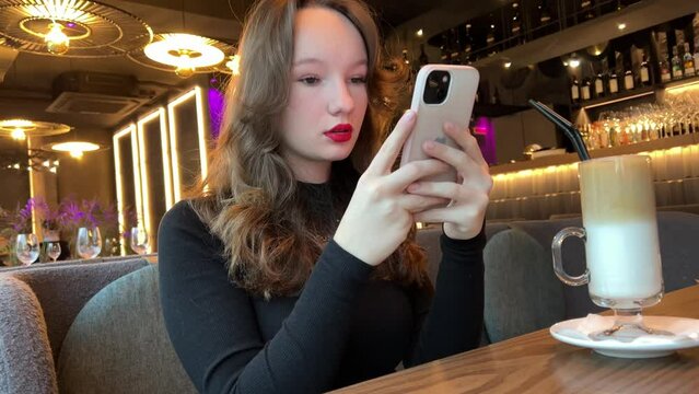 photo glass of latte Ice girl in restaurant making a video for social networks drinking drink beautiful people bright red lipstick black evening dress chic place for dinner. internet wi-fi addiction