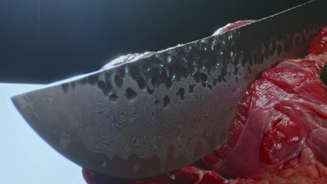A gloved chef cuts a piece of meat on a cutting board with a kitchen knife.