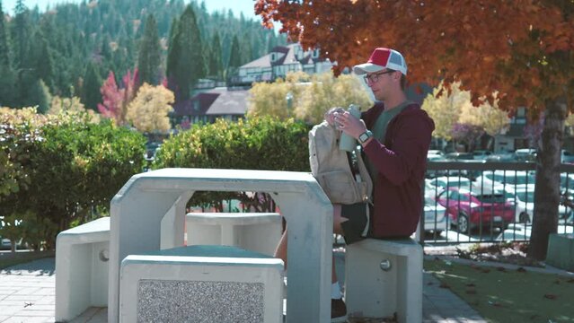 Hansom male hiker in casual attire adjusts his backpack with a peaceful autumn landscape and clear blue sky in the mountains behind him, sitting at the table and checking water thermos bottle. Hike 