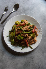 Top view of pan fried vegetables and chicken served in a white plate.
