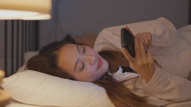 Asian woman secretly chatting to lover while lying in bed with husband.