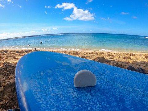 Surf wax on blue surf board on sandy beach by ocean
