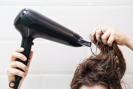 Young woman drying her hair with hairdryer in the bathroom close-up front view.