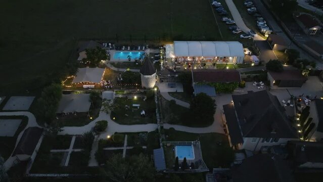Wedding venue glows under lights with outdoor hall radiant amid gardens, aerial