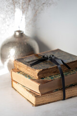 Closeup view of a stack of three antique books tied with a black ribbon, metallic vase blurred on the background