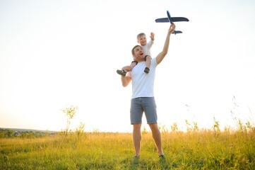 Cute little boy and his handsome young dad are smiling while playing with a toy airplane in the park.
