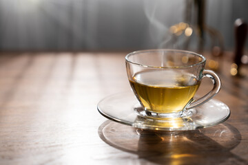 A hot tea cup emits smoke. It is placed on a wooden table with the morning sunlight shining on it.