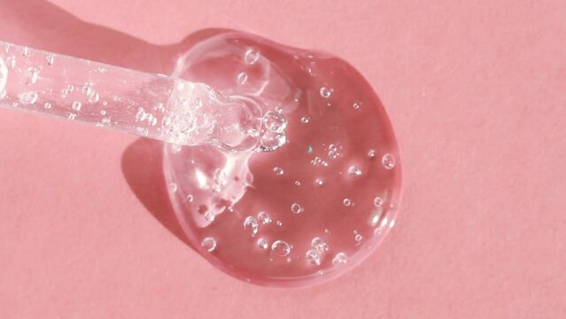 A drop of transparent cosmetic gel with bubbles on a pink background close-up. Dropper with emulsion in bright light.