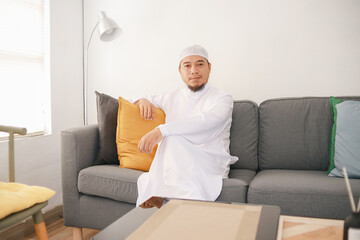 Portrait of smiling Asian man in white robe sitting on sofa at home