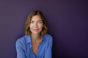 Pretty woman in blue blouse with short blonde hair looking at camera against a purple background