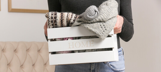 Woman holding wooden box with warm clothing items, donation and charity concept, domestic life,...