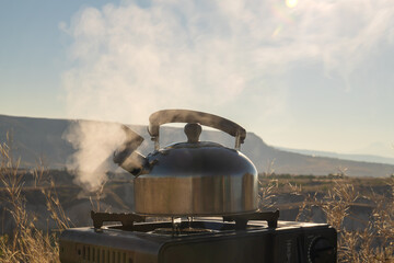 Close-up on a camping gas burner, a kettle boils early in the morning against the background of...