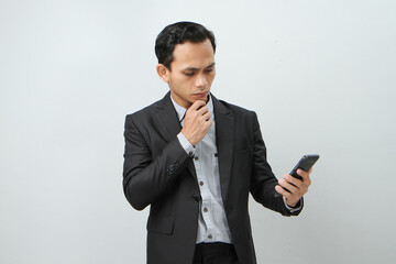 pensive asian indonesian business man in suit holding smart phone on isolated background