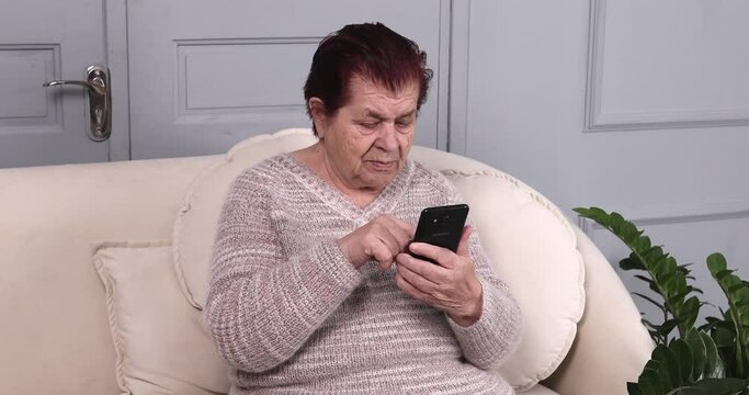 Happy smiling senior woman on pension rest on couch with smartphone scroll web pages swipe photos on dating website surf news at social media.