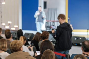 Defocused image of a speaker at event with audience watching intently, capturing the atmosphere of...