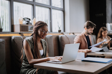 Beautiful businesswoman working on laptop in modern office. Group of freelancers working in shared work area. Concept of coworking, common workspaces for business, startups.