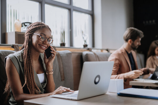 Beautiful businesswoman making phone call in modern office. Group of freelancers working in shared work area. Concept of coworking, common workspaces for business, startups.