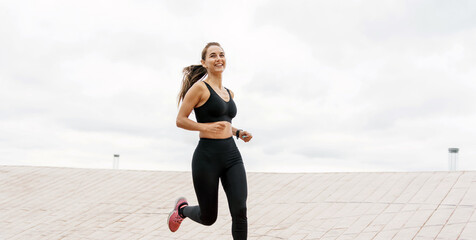 Energetic young woman running outdoors with cityscape in the background, cloudy sky.