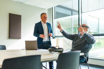 Manager using VR goggles next to employee in a office