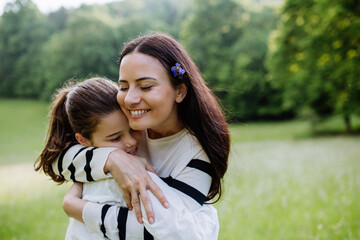 Beautiful mother with daughter, embracing, sitting in the grass at meadow. Concept of Mother's Day and maternal love.